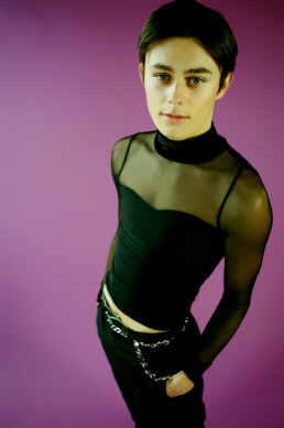Young male sitting on a stool against a purple backdrop.