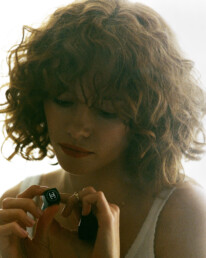 A curly red head young lady behind a foggy peice of glass smudged with bright red Chanel lipstick.