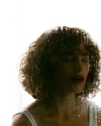 A curly red head young lady behind a foggy peice of glass smudged with bright red Chanel lipstick.