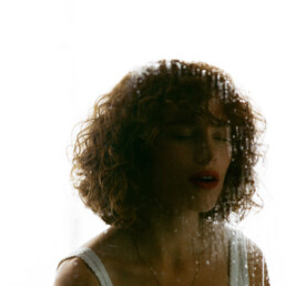 A curly red head young lady behind a foggy peice of glass smudged with bright red Chanel lipstick.