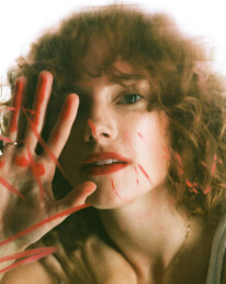 A curly red head young lady behind a foggy peice of glass smudged with bright red Chanel lipstick.